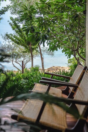 Eine Holzterrasse mit Korbstühlen mit Blick auf einen Strand.