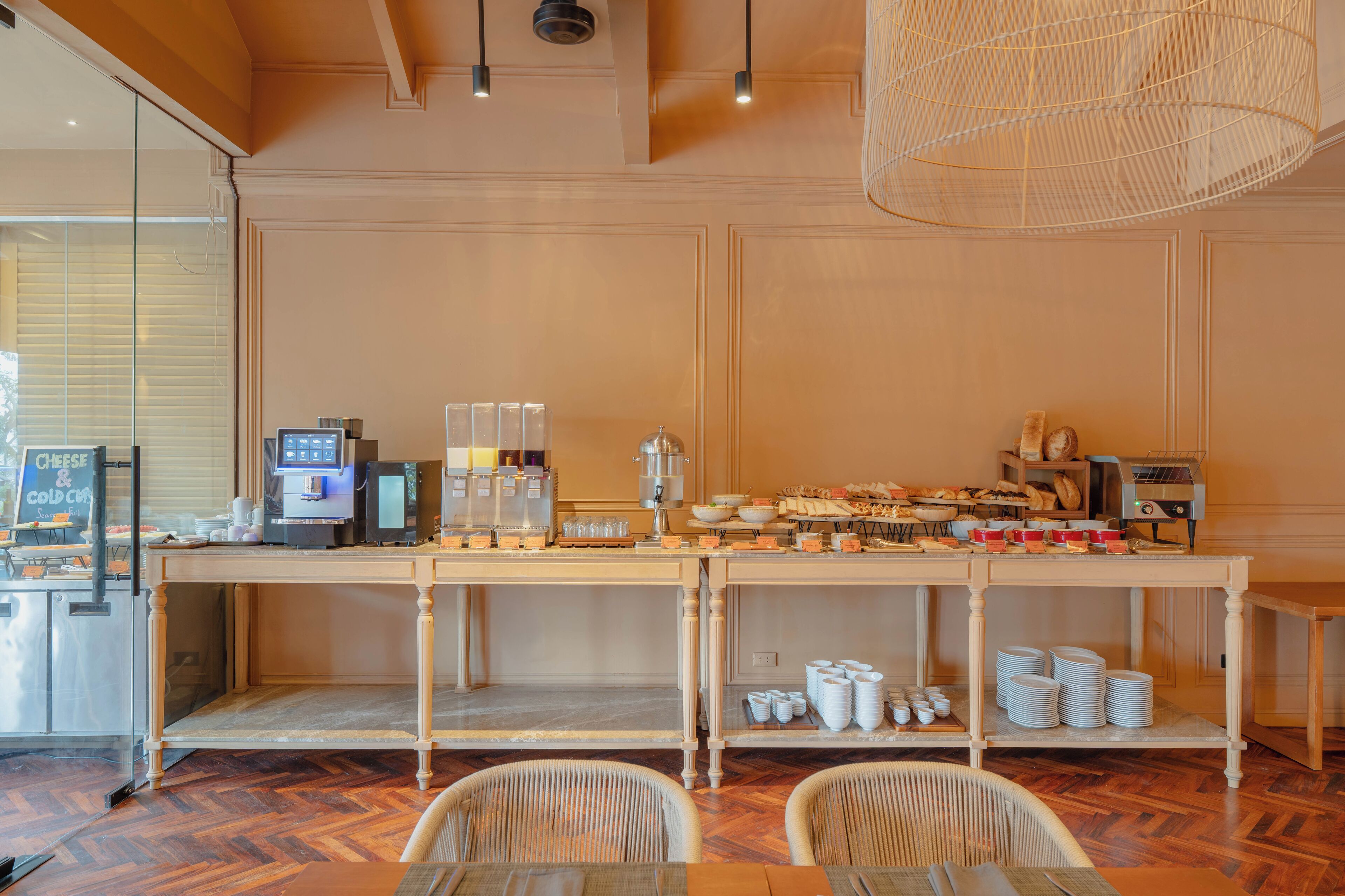 A buffet setup with a coffee machine, bowls, and plates on a wooden table.