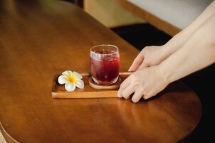 Una mesa de madera con un vaso de bebida roja y una flor blanca sobre un posavasos.