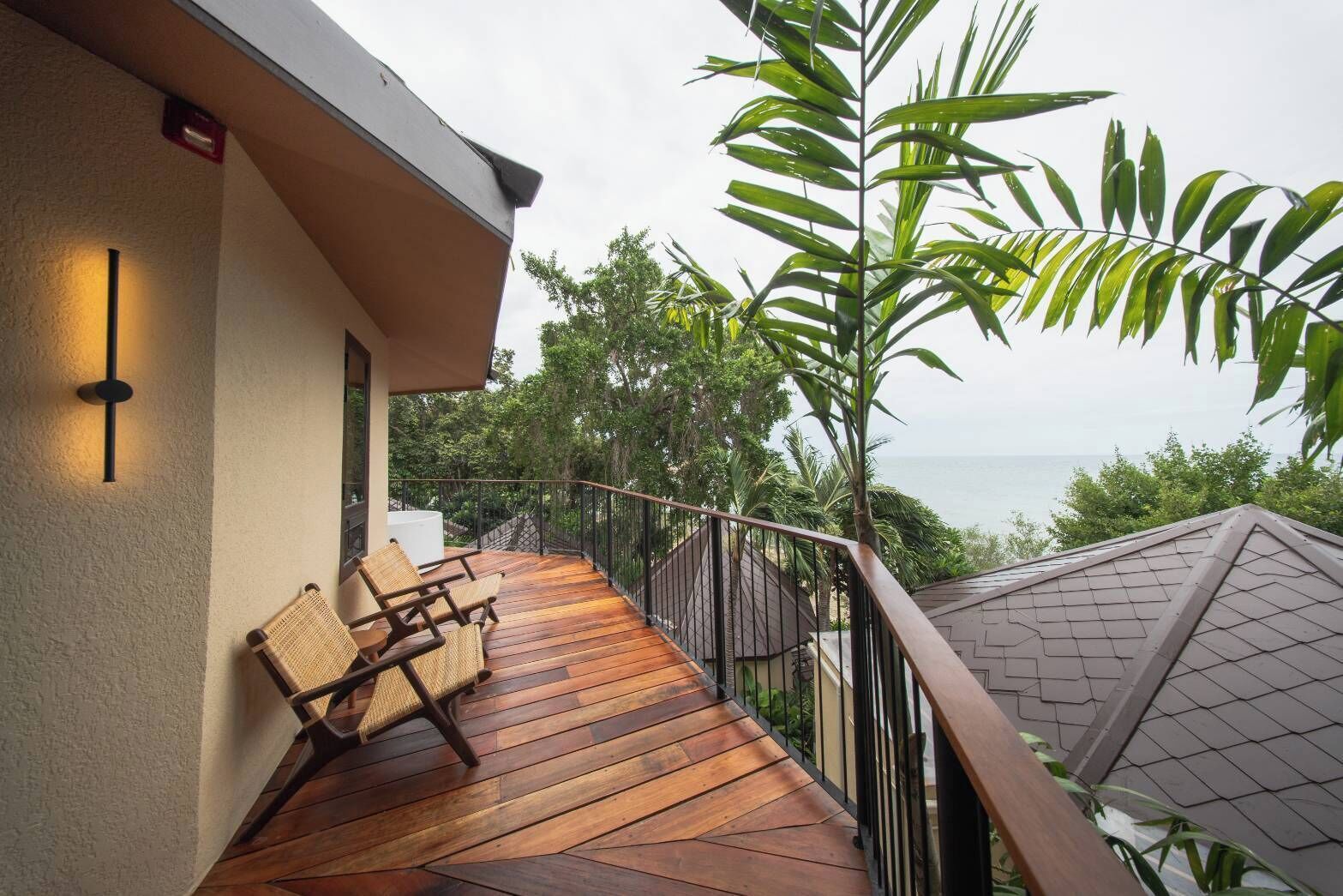 A wooden deck with two wicker chairs, a railing, and a view of the sea.