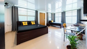 Una habitación de hotel moderna con una cama grande, un escritorio y una silla. Hay ventanas con cortinas, una planta en maceta y una puerta.