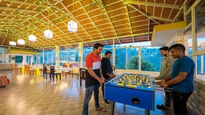 Un espacio interior amplio con mesa de futbolín, techo de madera y ventanas grandes.