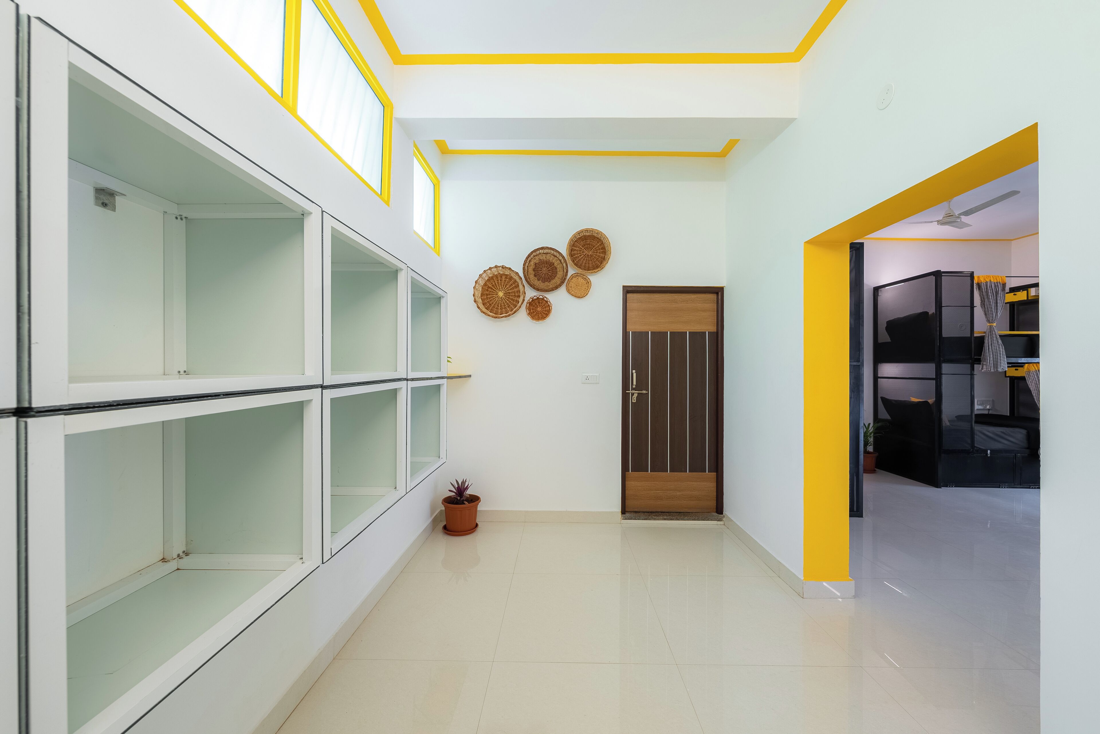 Un couloir aux couleurs blanche et jaune, avec une porte en bois et une plante en pot.