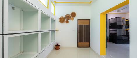 Un couloir aux couleurs blanche et jaune, avec une porte en bois et une plante en pot.