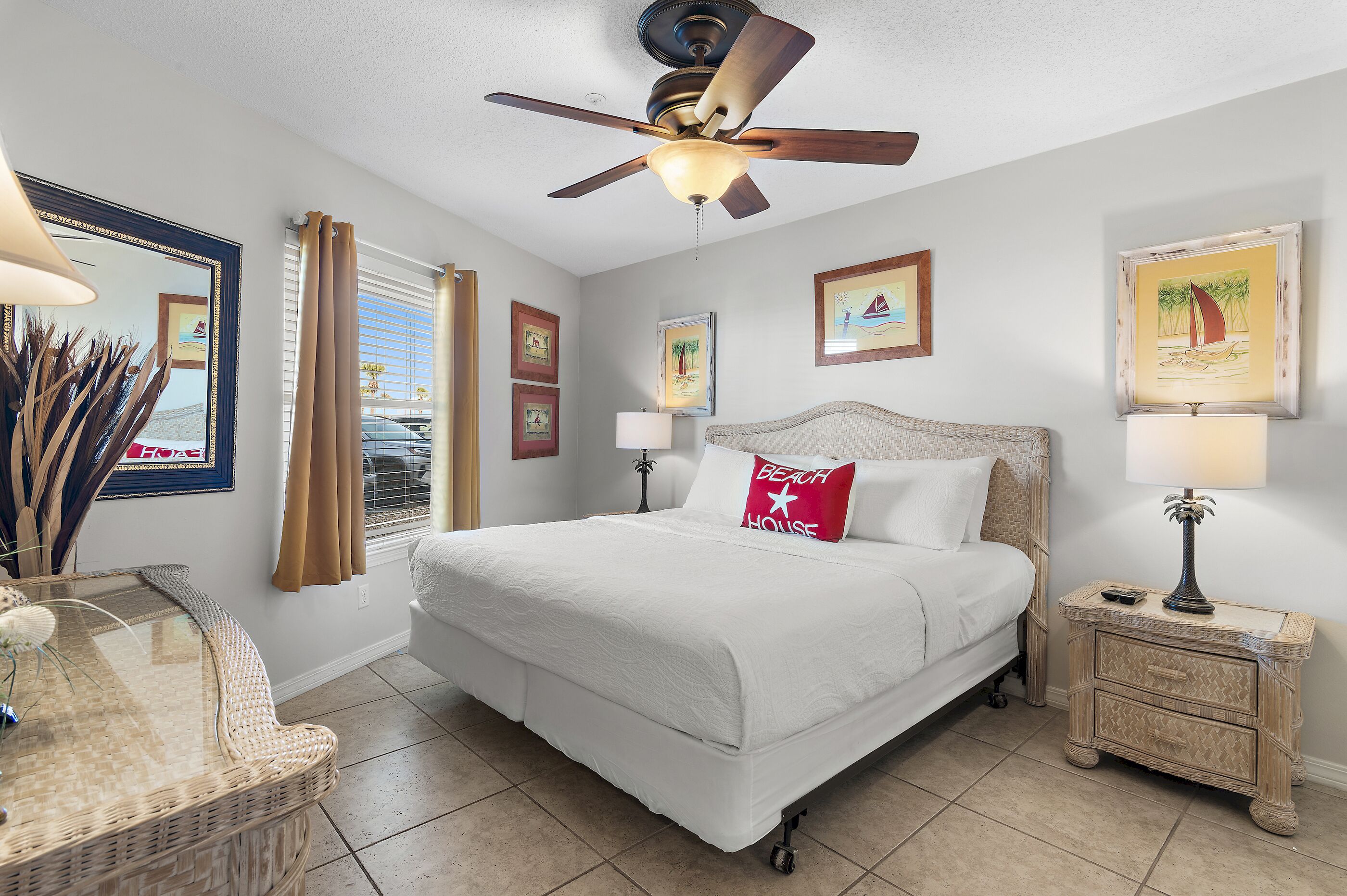 A hotel room with a large bed, a ceiling fan, a nightstand with a lamp, and framed pictures on the walls.