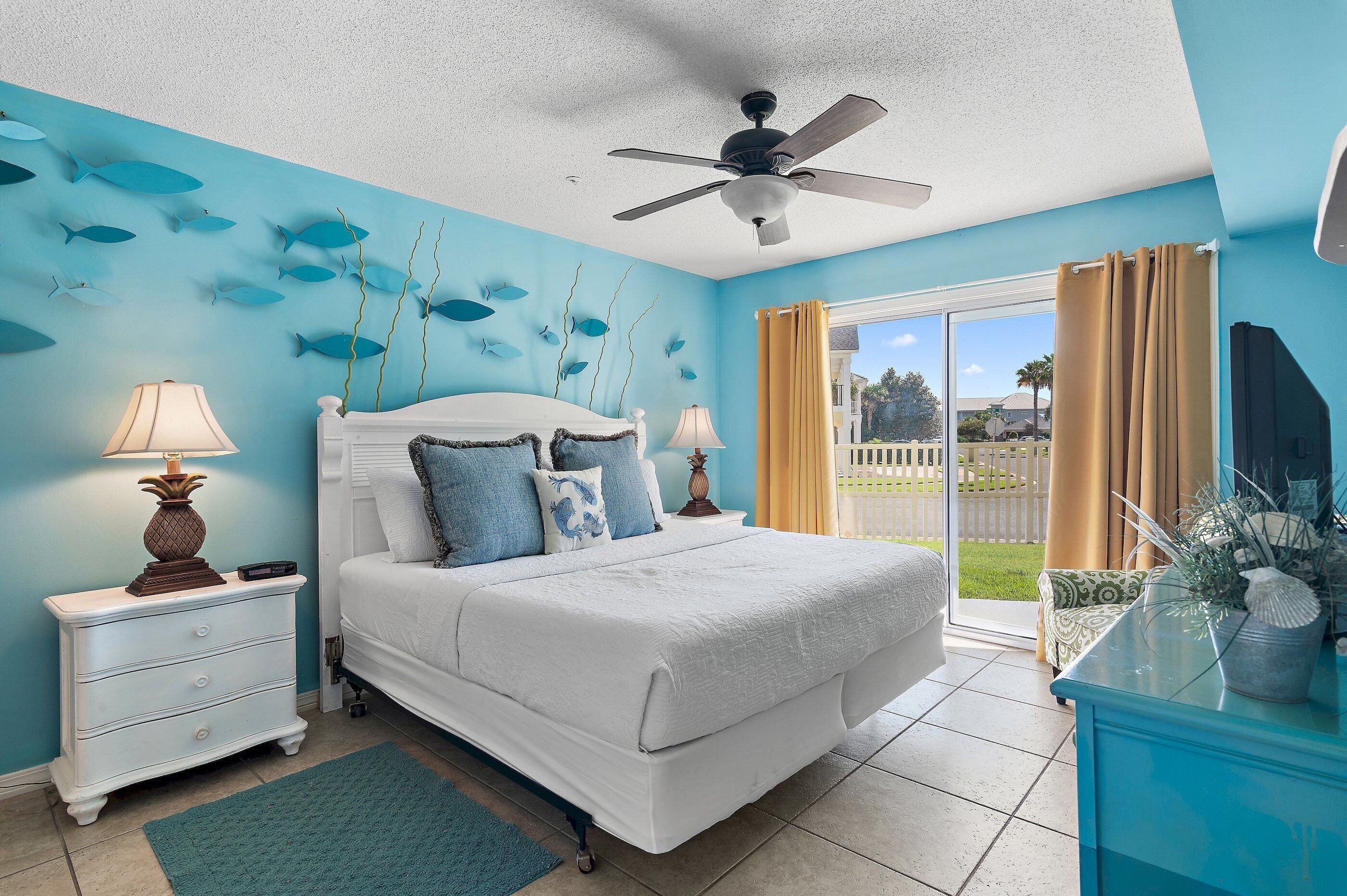 A bedroom with a bed, nightstands, a ceiling fan, and a view of the outdoors.