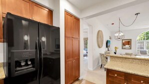A kitchen with a black refrigerator, wooden cabinets, and a granite countertop. - Desert Charm A | 1BR Legacy Villa (La Quinta)