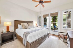 Ein Schlafzimmer mit einem großen Bett, einem Deckenventilator und Blick ins Freie durch eine Schiebetür.