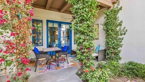 A covered patio with a table and chairs, a blue door, and a wall covered in climbing plants. - Desert Charm A | 1BR Legacy Villa (La Quinta)