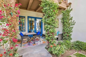 A covered patio with a table and chairs, a blue door, and a wall covered in climbing plants. - Desert Charm A | 1BR Legacy Villa (La Quinta)