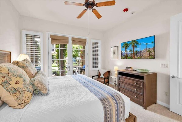A bedroom with a bed, a ceiling fan, a dresser, a TV, and a painting.