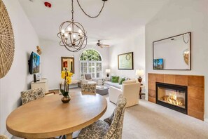 A dining area with a round table, chairs, a chandelier, and a fireplace.