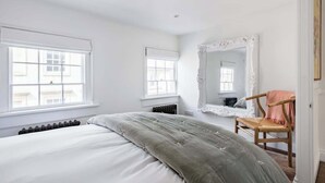 Ein Schlafzimmer mit einem Bett, zwei Fenstern, einer Heizung, einem Spiegel und einem Sessel.