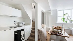 Eine moderne Küche mit weißen Schränken, einem eingebauten Backofen und einem Essbereich mit Holztisch und einem Fenster mit Pflanze.