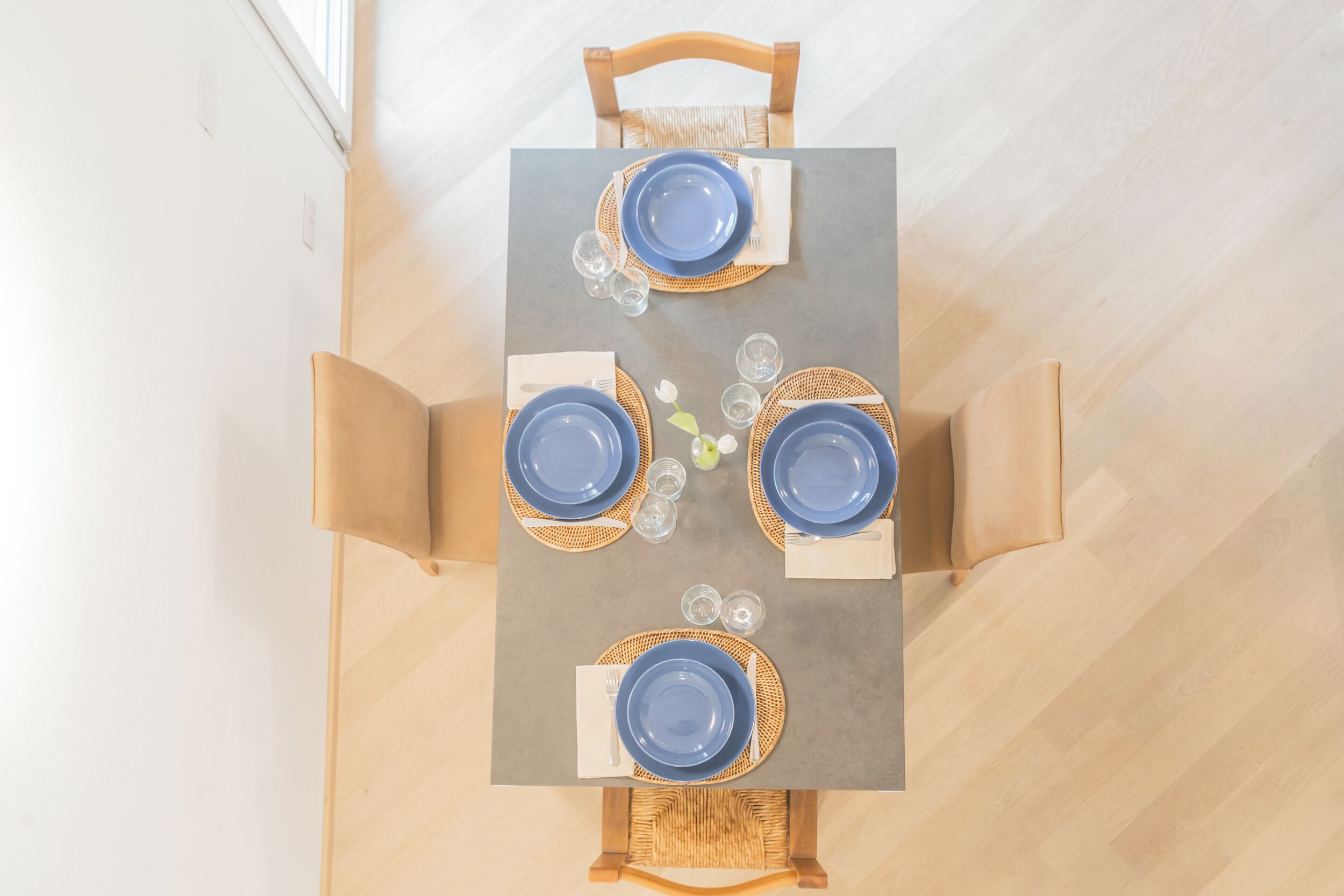 A dining table set for four with blue plates, white napkins, and glassware.