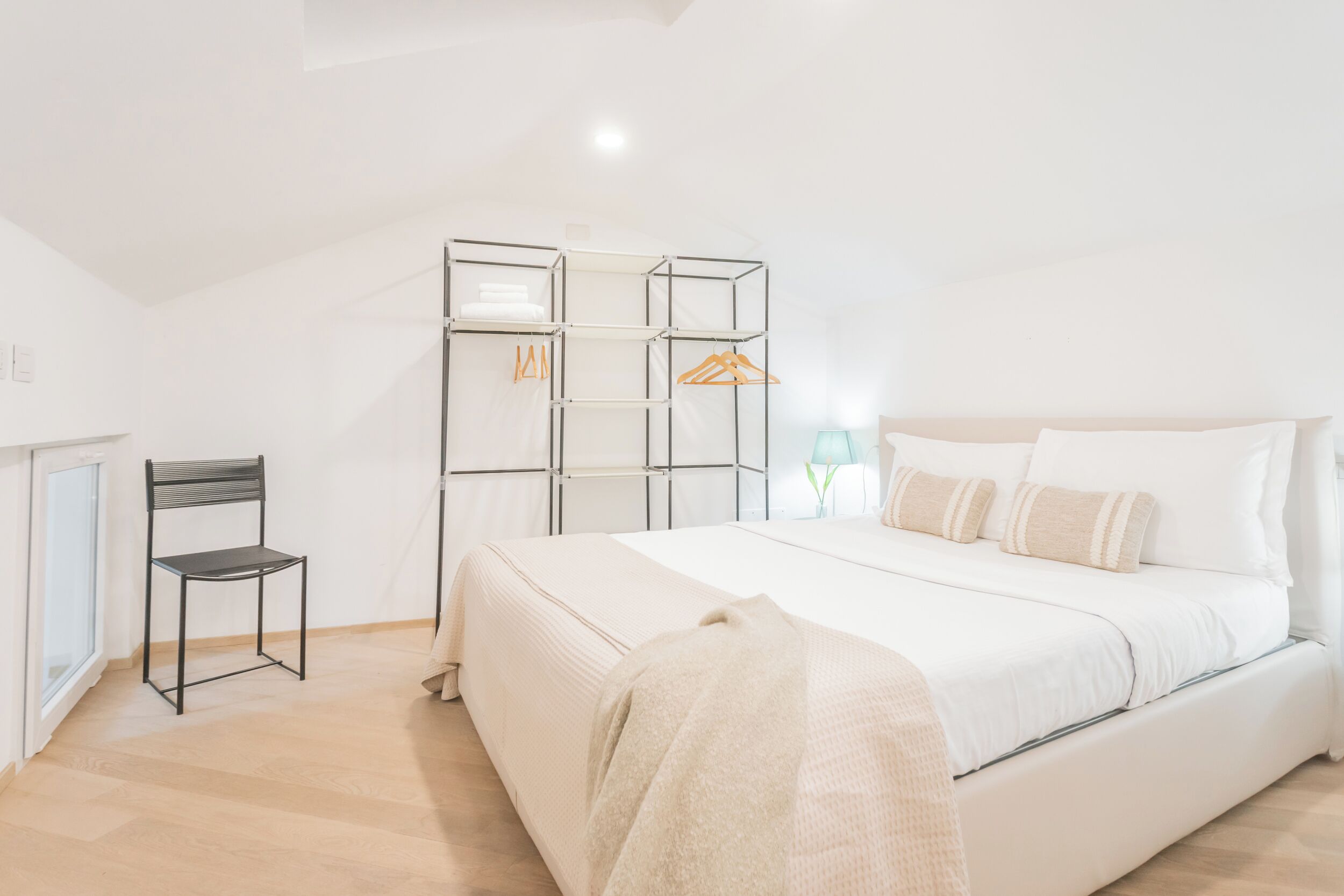 A modern bedroom with a large bed, a chair, a wardrobe, and a desk.