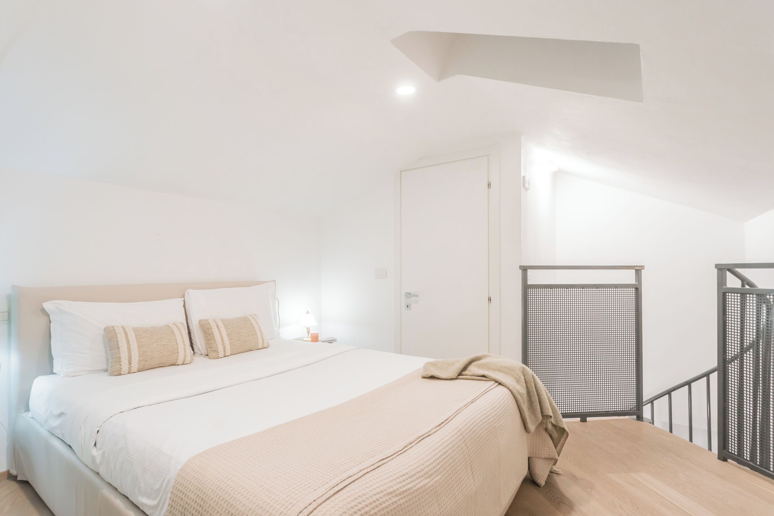 Een slaapkamer met een bed, nachtkastje, lamp, deur en een trap met leuning.