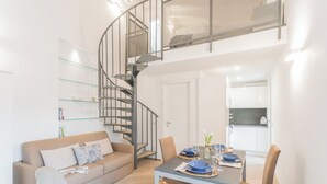Una sala de estar moderna con una escalera espiral, un comedor con una mesa dispuesta para dos personas, y una cocina al fondo.