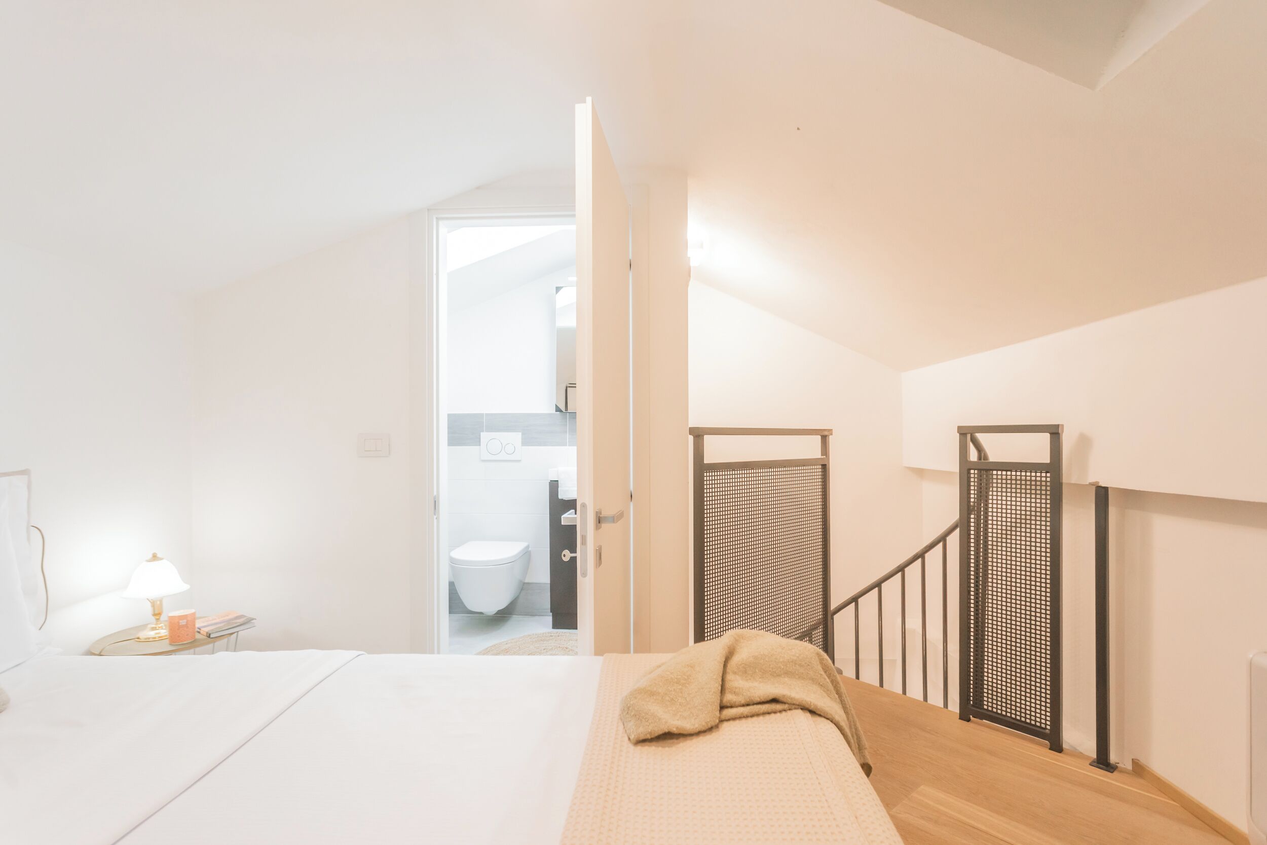 Une chambre à coucher avec un lit, une table de chevet avec une lampe, et une vue sur une salle de bain par une porte ouverte.