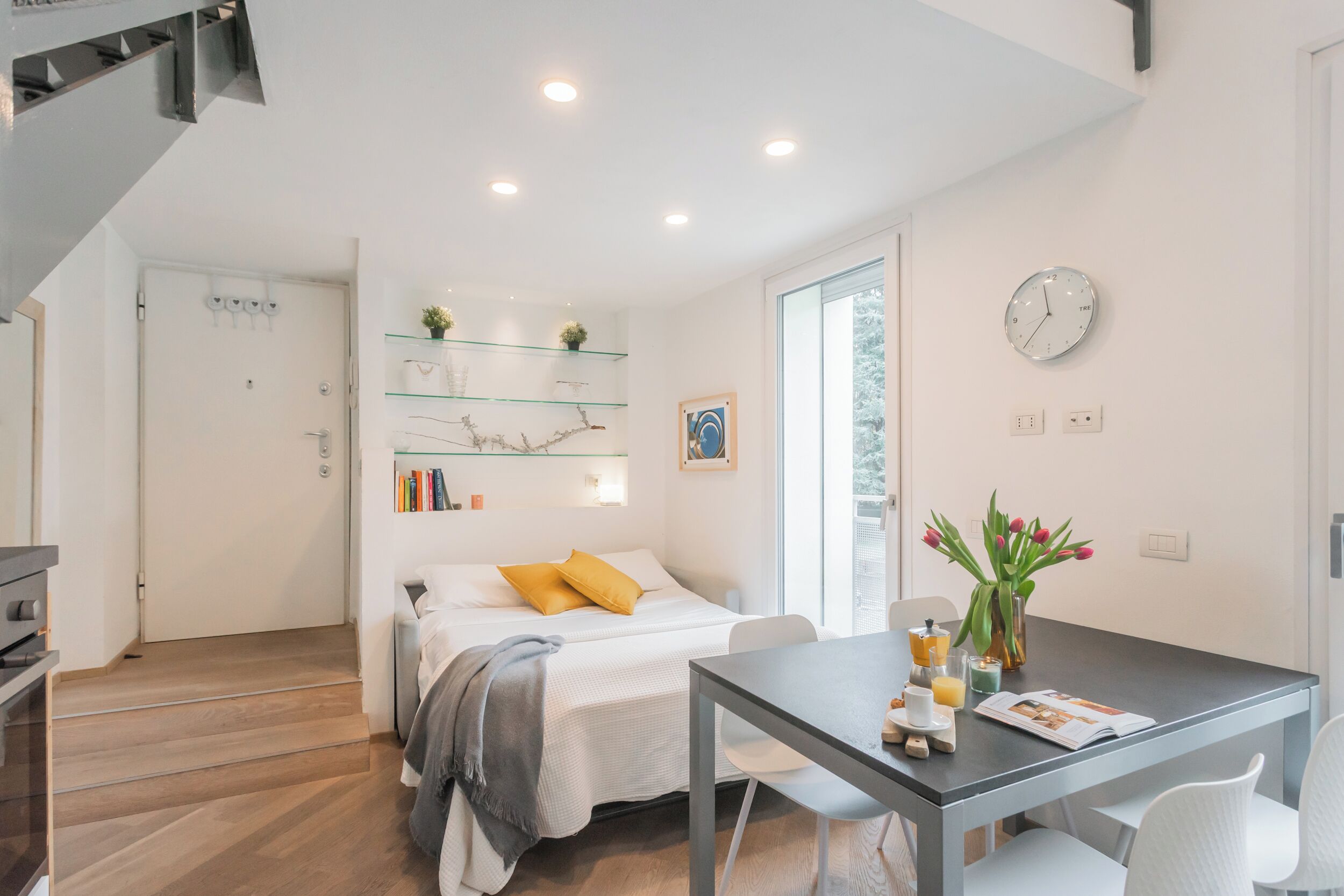 A modern bedroom with a bed, bedside table, and a glass shelf with books and decorative items.
