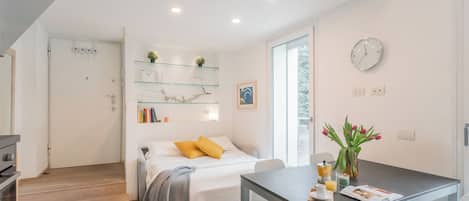 A modern bedroom with a bed, bedside table, and a glass shelf with books and decorative items.