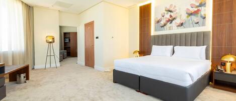 A hotel room with a large bed, bedside lamps, a painting on the wall, and a desk with a lamp.