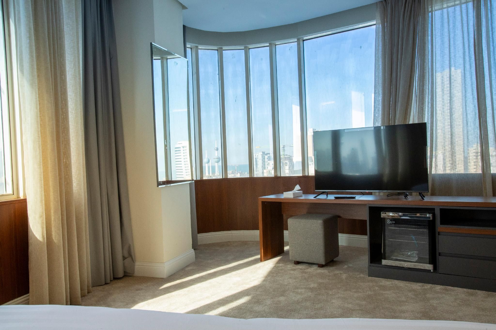 Ett hotellrum med ett stort fönster, en platt-TV, ett skrivbord och en minibar.