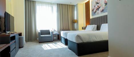 A hotel room with a large bed, two bedside tables, a desk with a chair, a TV, and a large window with curtains.
