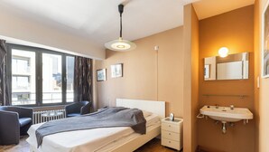 Habitación de hotel con cama, mesita de noche, lámpara y baño con lavamanos y espejo.