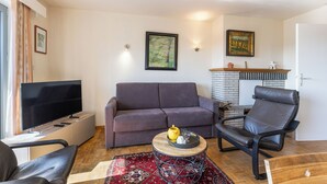Una sala de estar con un sofá, una silla, un televisor, una chimenea y un cuadro en la pared.