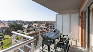Un balcón con mesa y sillas, con vista a una zona residencial con casas y árboles.