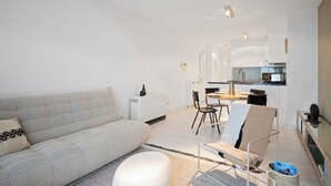 A modern living room with a sofa, a coffee table, and a dining area with chairs and a table.