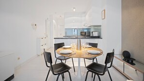 A modern kitchen with white cabinets, a central island, and a dining area with a round table and black chairs.