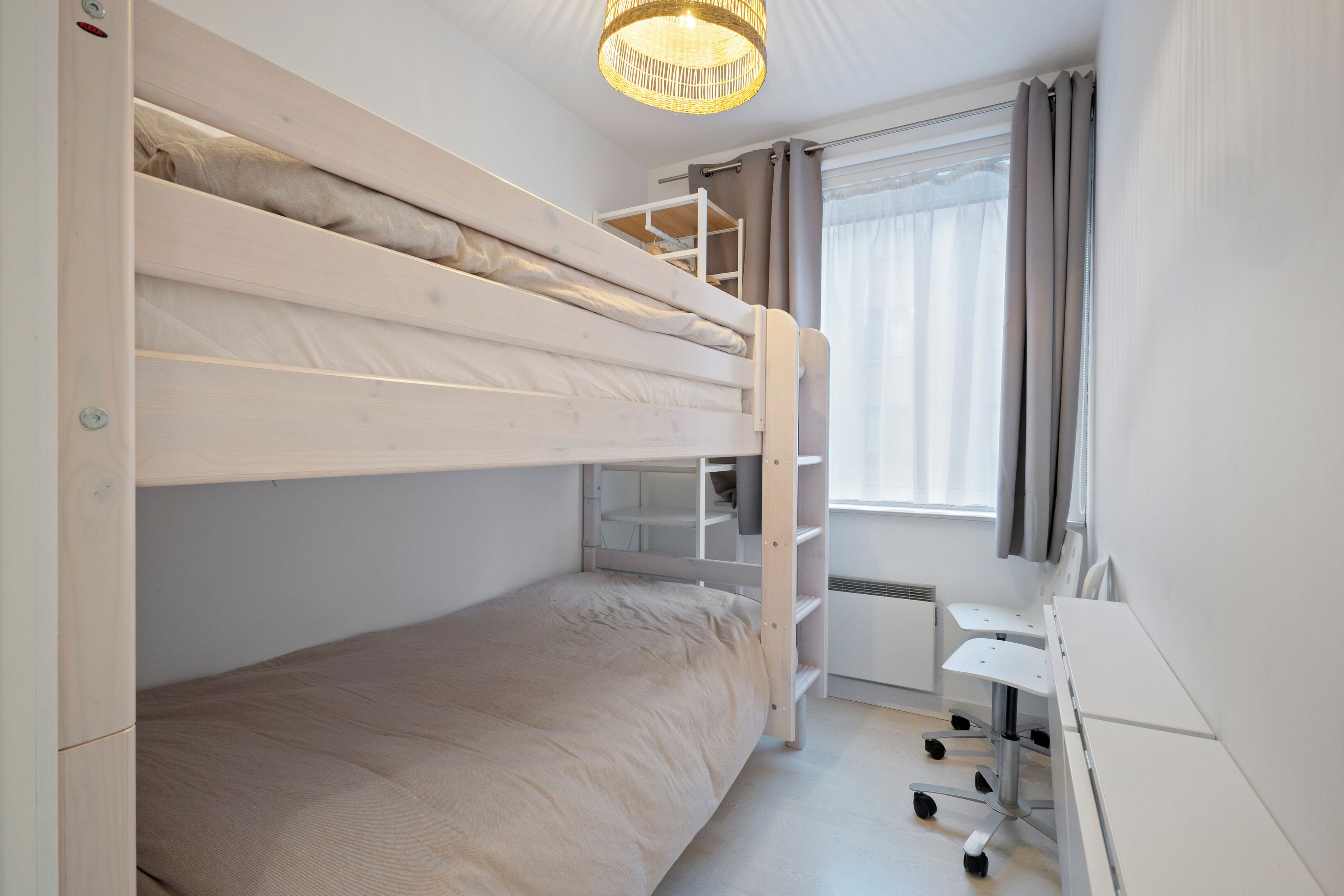 A bunk bed room with a desk and chair, a window with curtains, and a hanging light fixture.