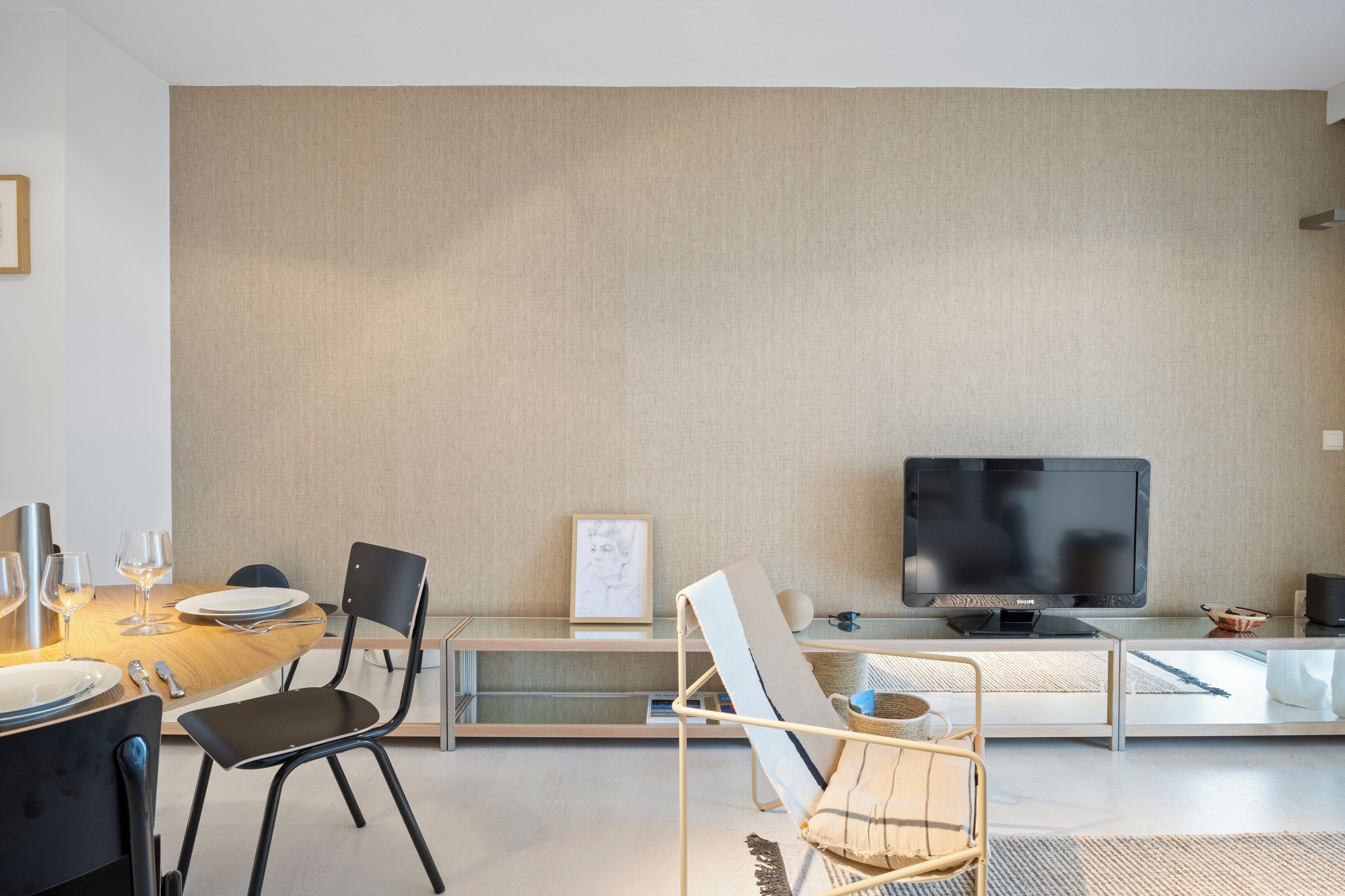 A modern living room with a flat-screen TV, a dining table with chairs, and a sofa.