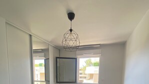 A bedroom with a bed, a geometric pendant light, a window, and a mirror on the wall. - Le Refuge du Plongeur - New & Cosy Apartment (Saint-Mandrier-sur-Mer)