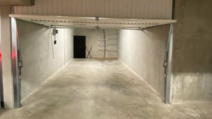 A spacious, empty garage with concrete floors and walls, a metal door, and a ladder against the back wall. - Le Refuge du Plongeur - New & Cosy Apartment (Saint-Mandrier-sur-Mer)