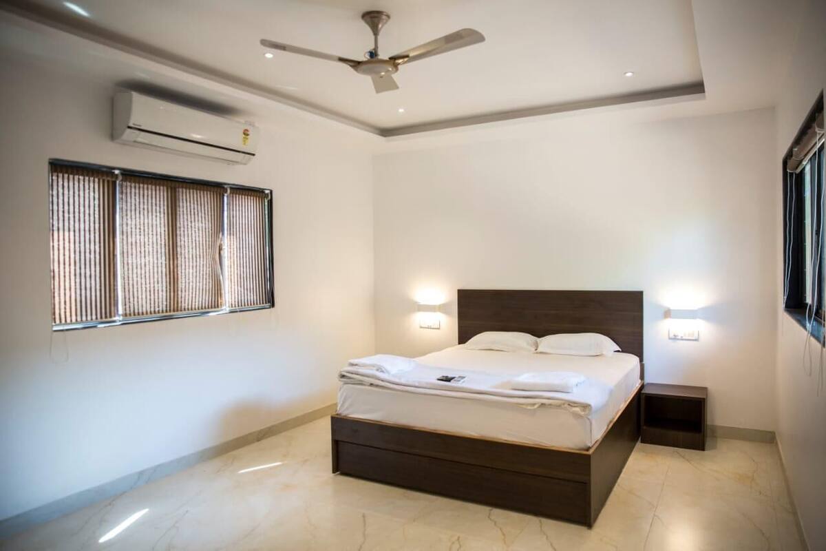 A modern bedroom with a bed, ceiling fan, air conditioning unit, and window with blinds.