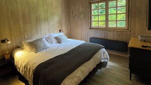 Un dormitorio con paneles de madera, una cama grande, una lámpara colgante, una ventana con vistas a la vegetación y un aparador.