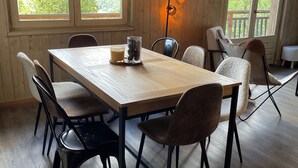 Una habitación con paneles de madera, una mesa grande y sillas, una lámpara de pie y vistas al exterior a través de amplios ventanales.