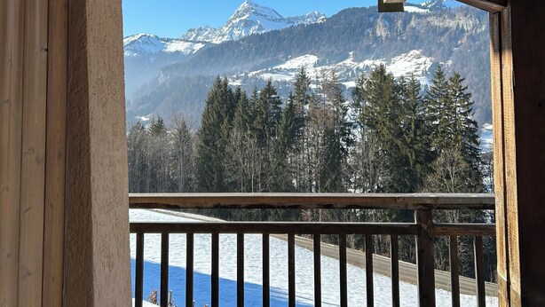 Un balcón de madera con vistas a montañas nevadas y un cielo azul despejado.