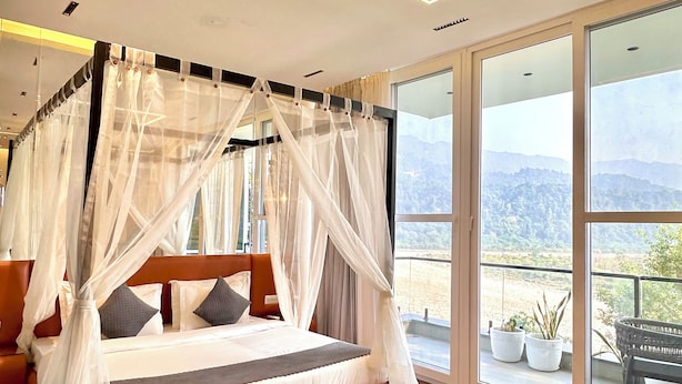 Une chambre avec un lit à baldaquin, un plancher en bois et une vue sur l’extérieur.