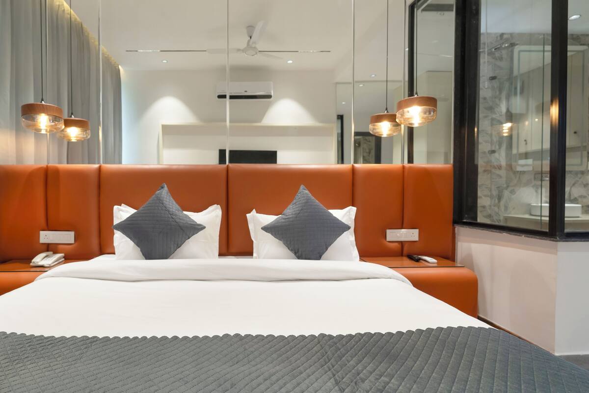 Une chambre d’hôtel moderne avec un grand lit, une tête de lit orange et deux lampes de chevet.
