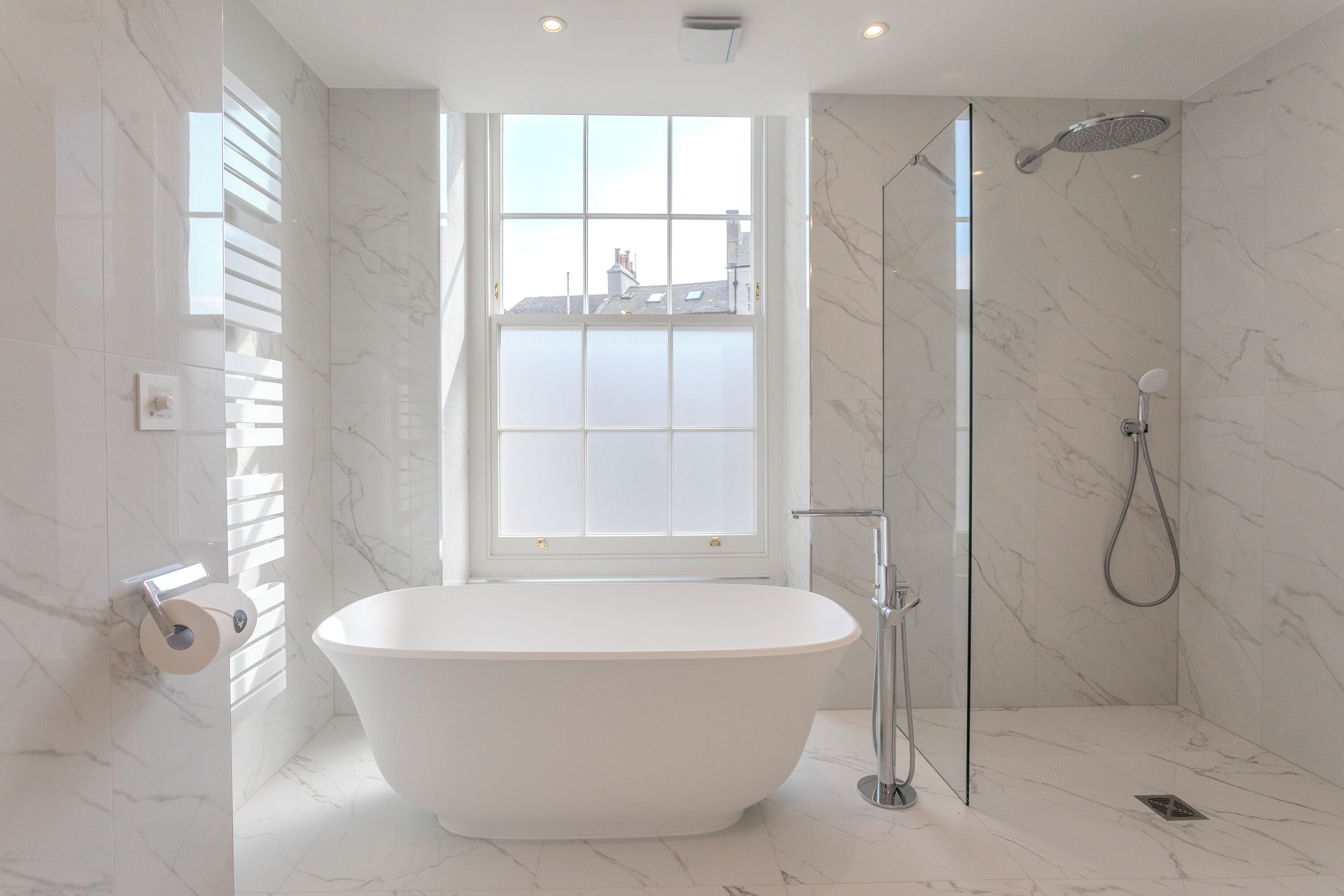 A modern bathroom with a freestanding bathtub, a glass-enclosed shower, and a large window providing natural light.