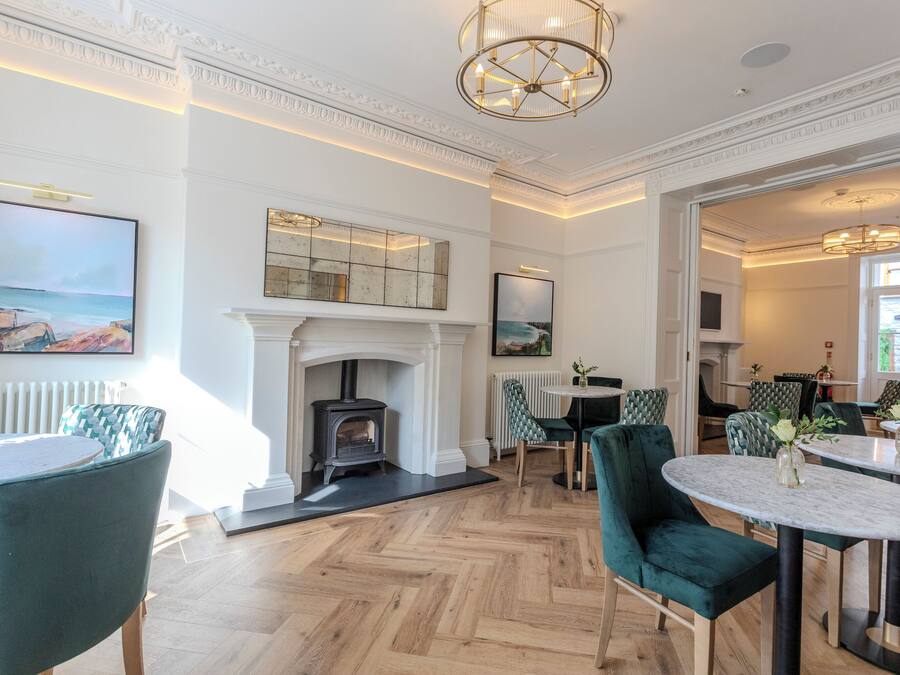 A spacious room with a fireplace, green upholstered chairs, and a herringbone wood floor.