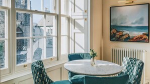 A dining area with a round table, four chairs, and a painting on the wall. - Suites at Derby House (Castletown)