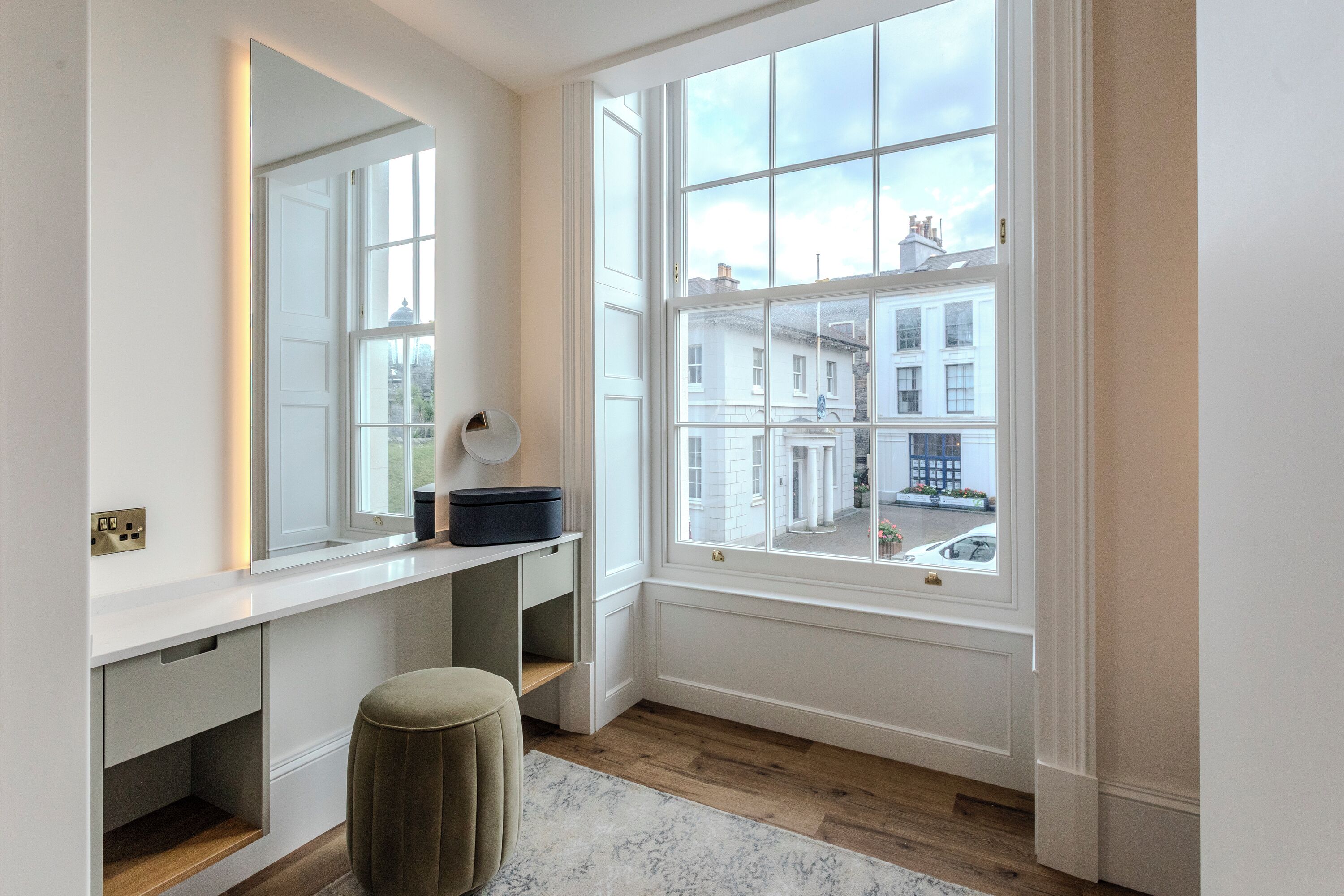 A modern bathroom with a large window, a vanity with a mirror, and a wooden floor.