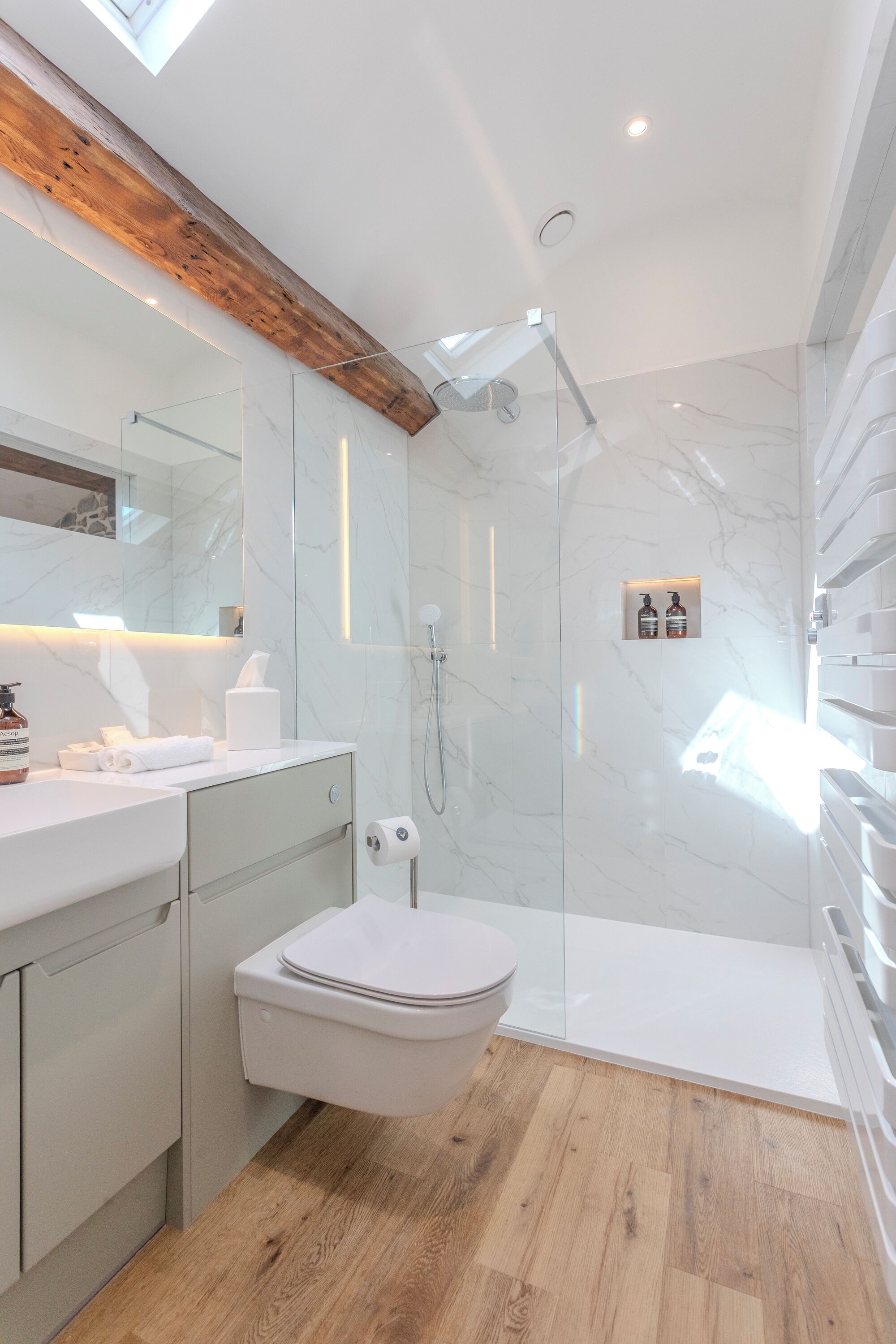 A modern bathroom with a glass-enclosed shower, a wooden beam ceiling, and a marble backsplash.
