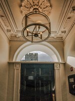Una entrada imponente con una puerta negra, un techo ornamentado y vistas a un castillo a través de un arco.