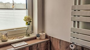 A bathroom with a wooden vanity, a window with blinds, a hanging light fixture, a small vase with a flower, a tissue roll, and a soap dish. - Cosy apartment for 2 people with WIFI, TV and terrace (Schieder-schwalenberg)